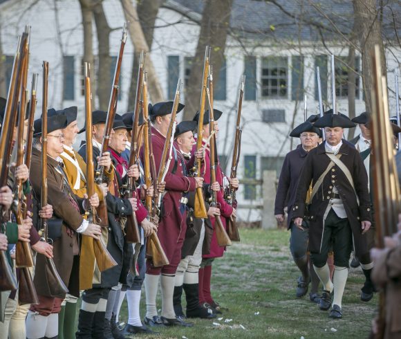 Reenactment of the battle at Lexington, men dressed in wool coats holding guns at solute